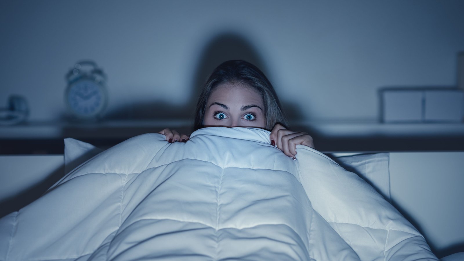 woman watching scary movie in bed horror