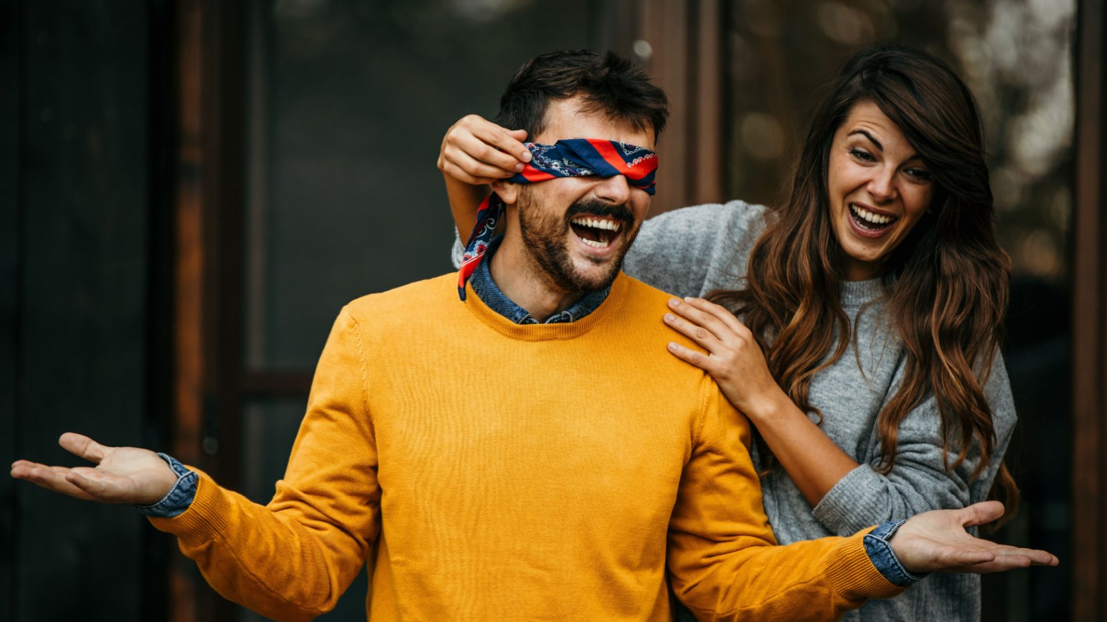 A woman blindfolds her boyfriend in a birthday friends surprise him La Famiglia Shutterstock