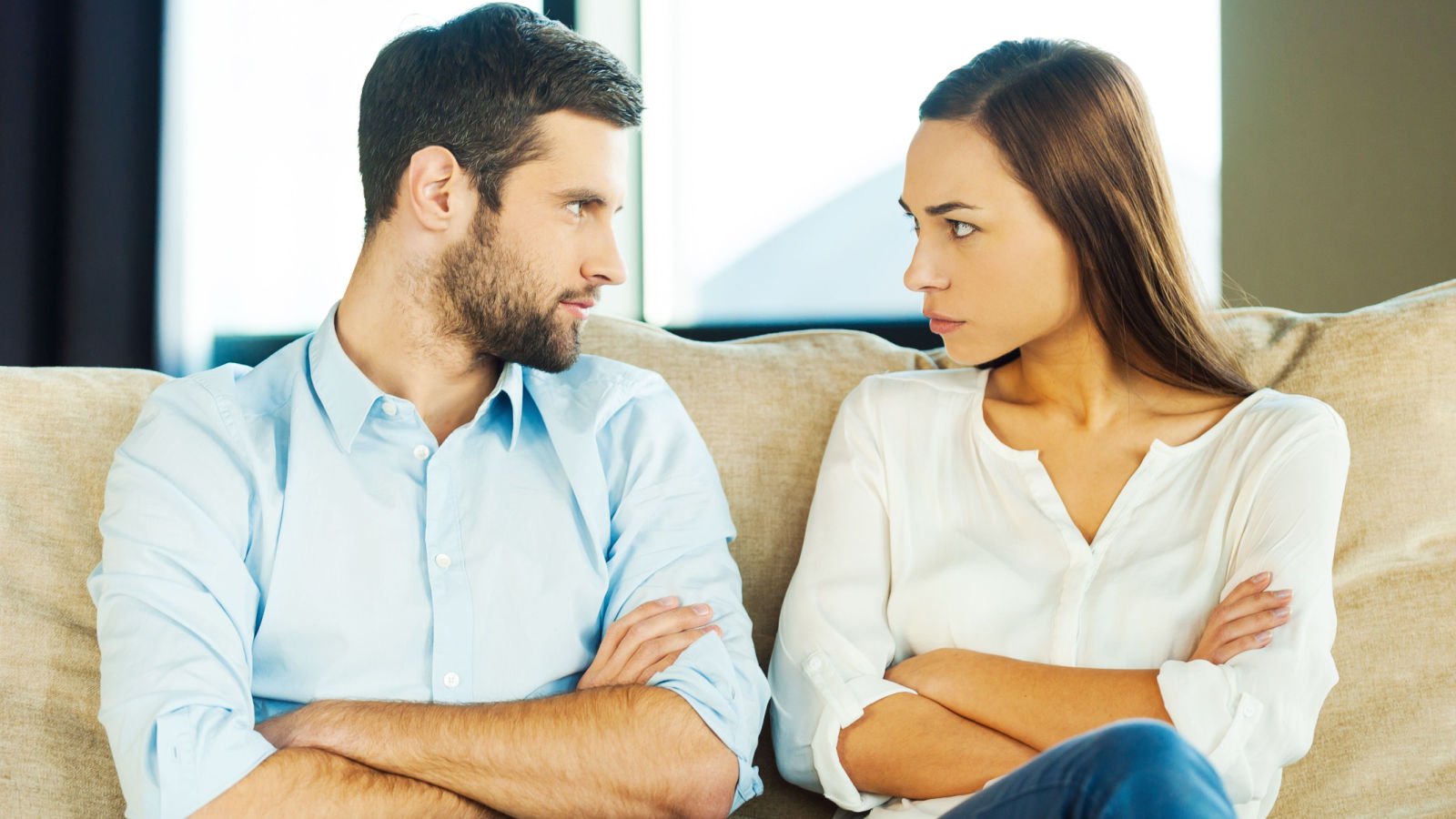 Angry young couple looking at each other and keeping arms crossed fighting