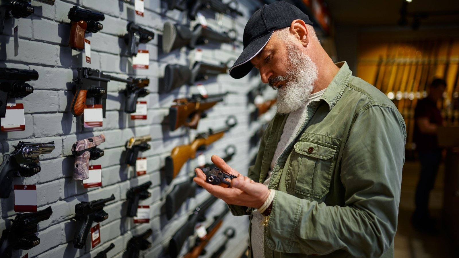 Bearded man holds pistol at showcase in gun store firearm shop weapon Nomad Soul Shutterstock