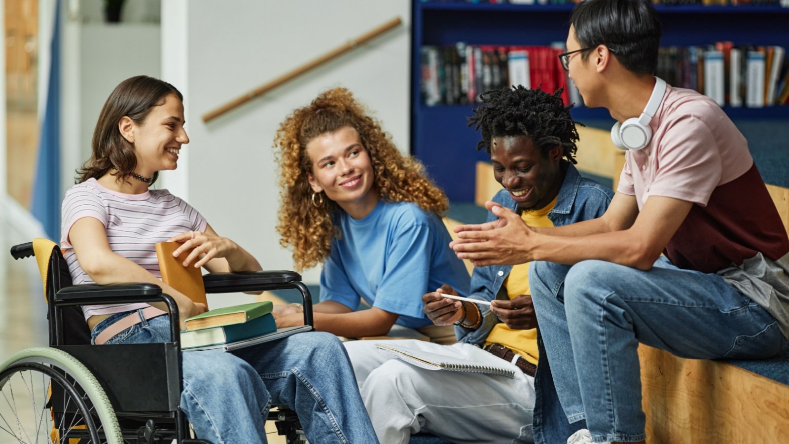 Diverse group of young people chatting in college library including female student with disability SeventyFour Shutterstock