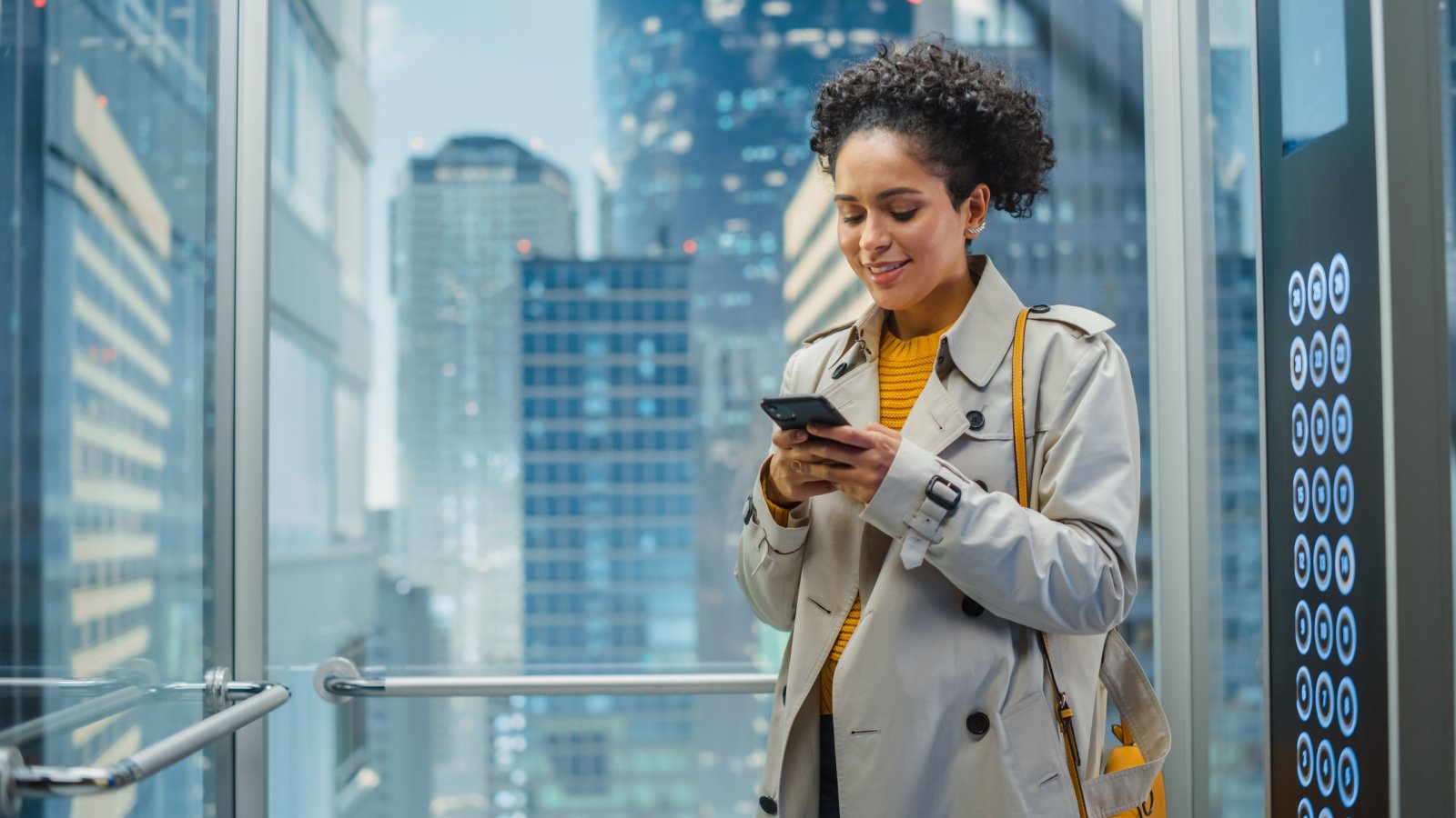 Glass Elevator to Office in Modern Business Center. Successful Manager Smile while Using Smartphone Gorodenkoff Shutterstock