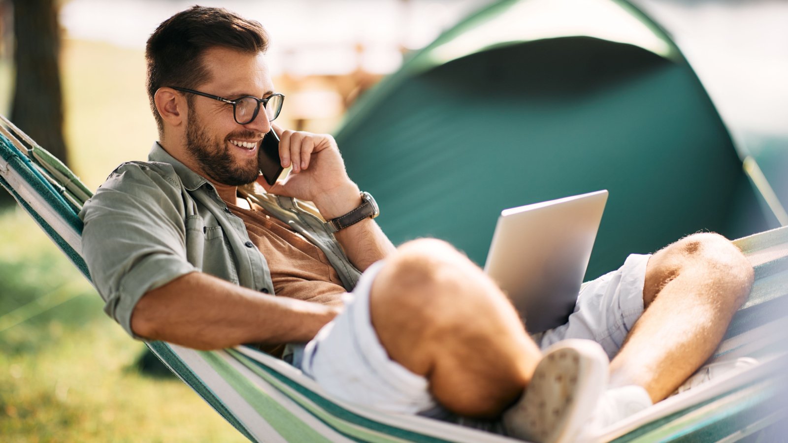 Happy entrepreneur relaxing in hammock while using laptop and making call during camping day hammock camping drazen zigic shutterstock