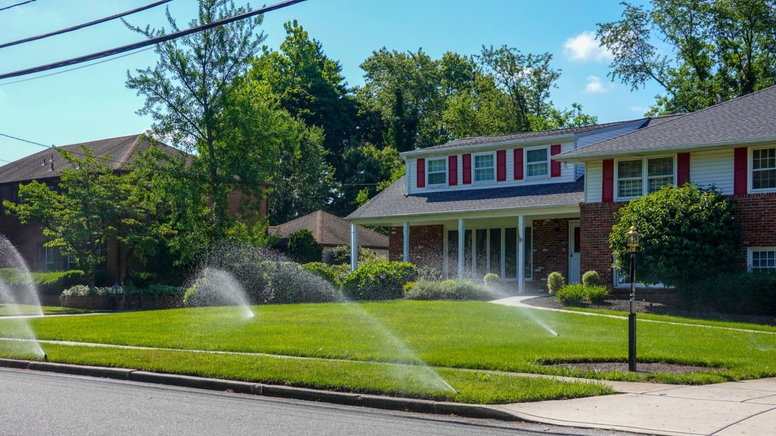 Lawn irrigation sprinklers water garden green grass lawn in front of a suburban house home Alan Budman Shutterstock