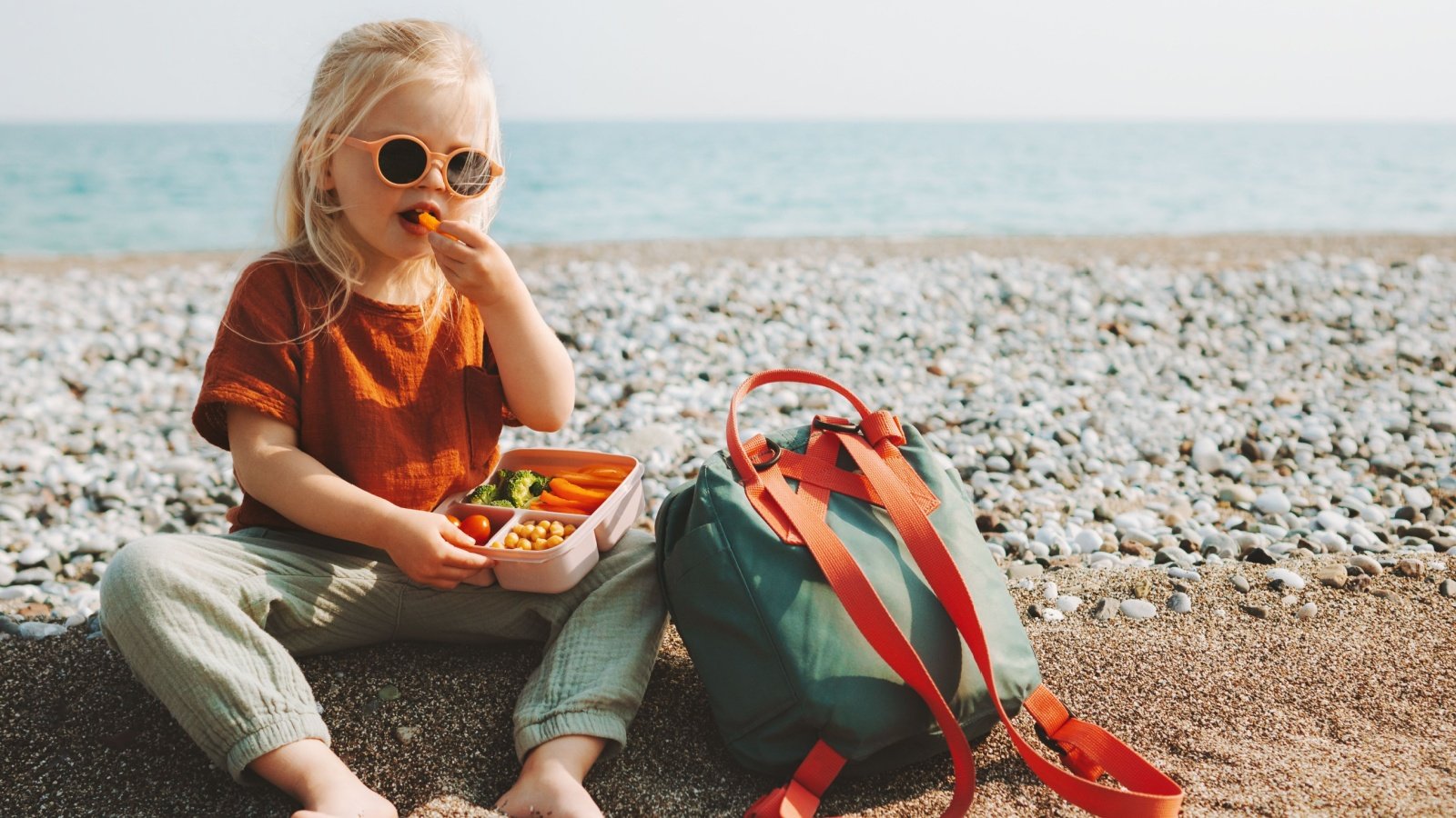 Lunch box backpack kid child girl eating outside on the beach everst Shutterstock