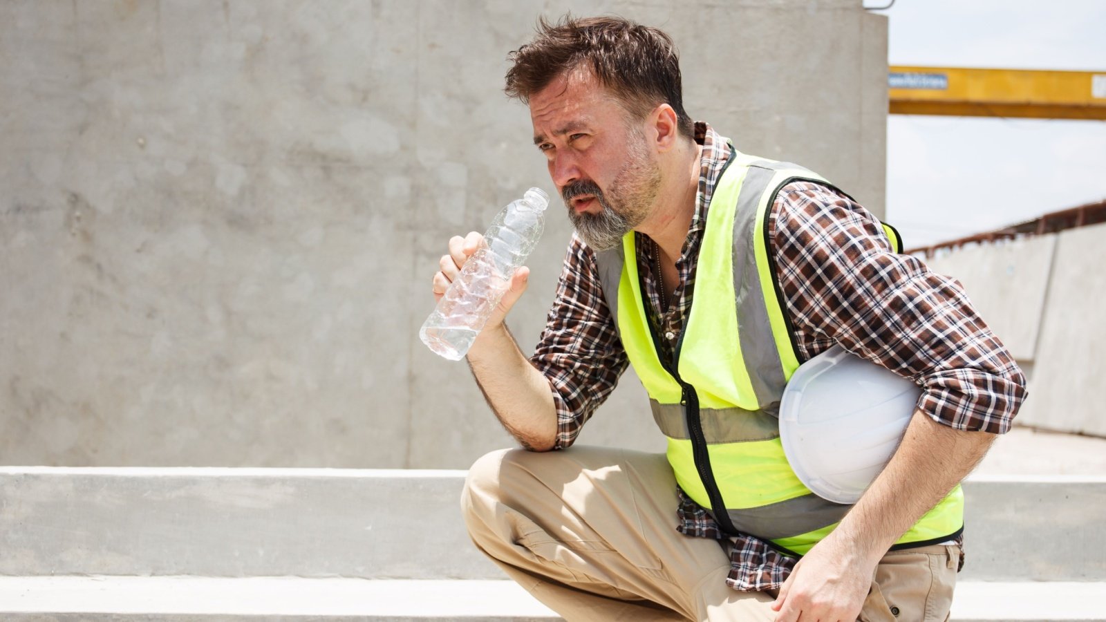 Male construction worker resting and drinking water bottle hot day heat exhaustion wave extreme DG FotoStock Shutterstock