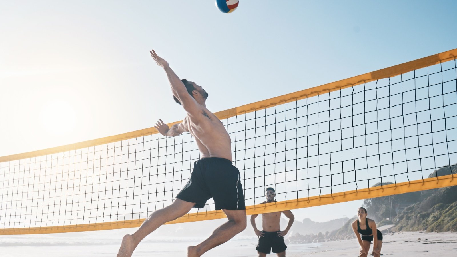 Male jump and volleyball in air on beach by net sport play PeopleImagescom Yuri A Shutterstock