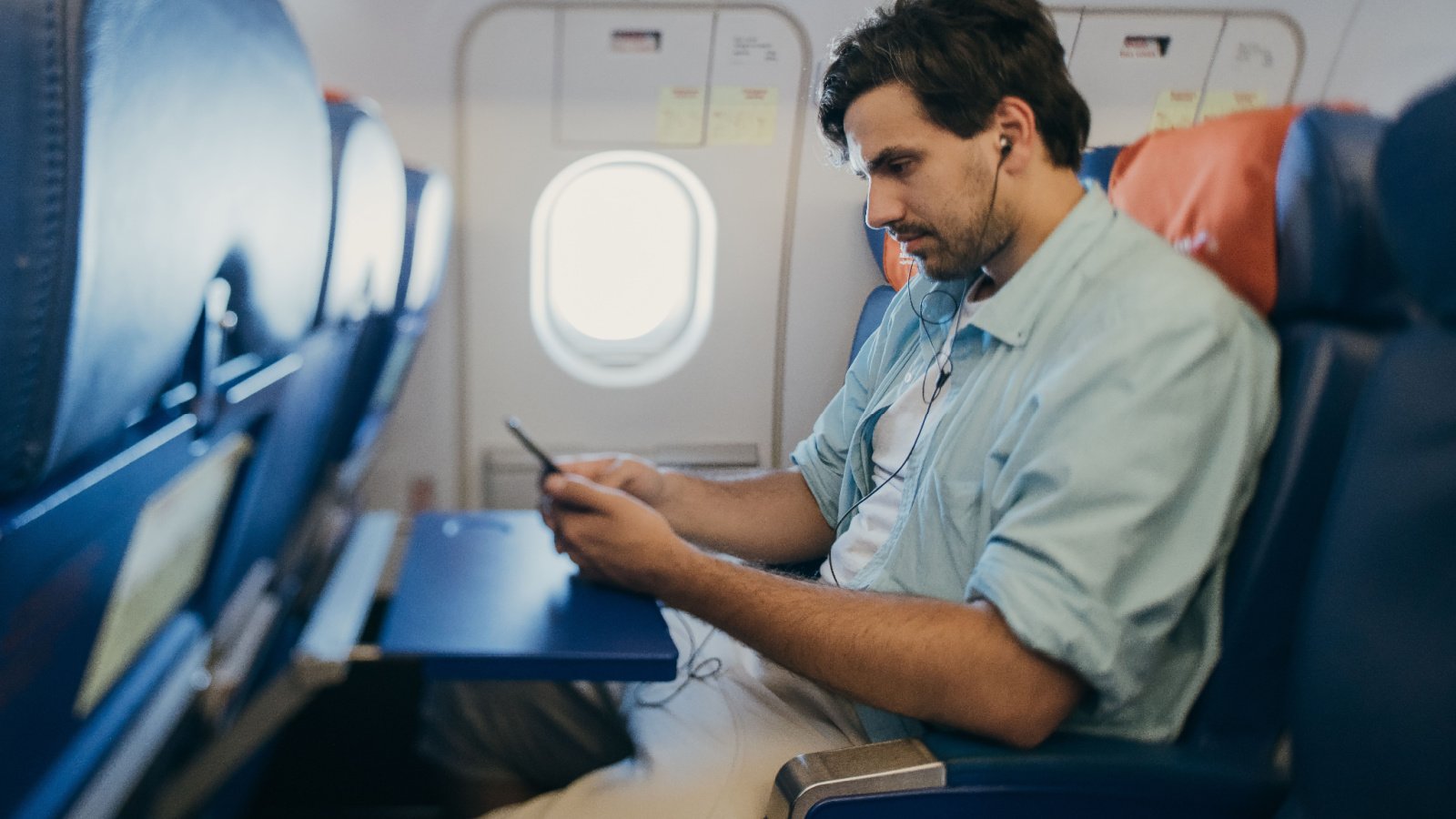 Male middle seat Airplane music headphones phone Grusho Anna Shutterstock