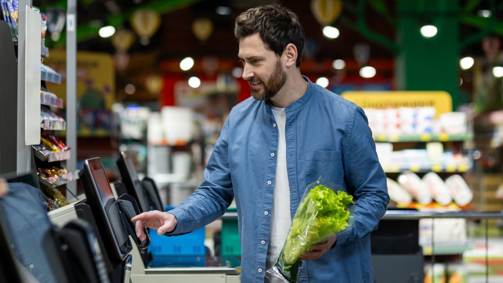 Male uses self checkout machine in a supermarket grocery store shop holding lettuce voronaman Shutterstock