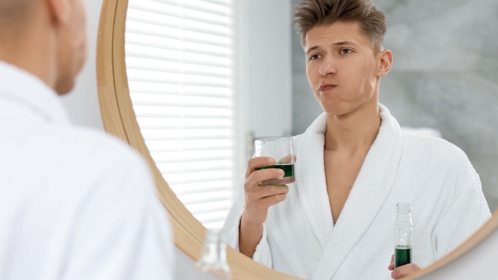 Male using mouthwash near mirror in bathroom New Africa Shutterstock