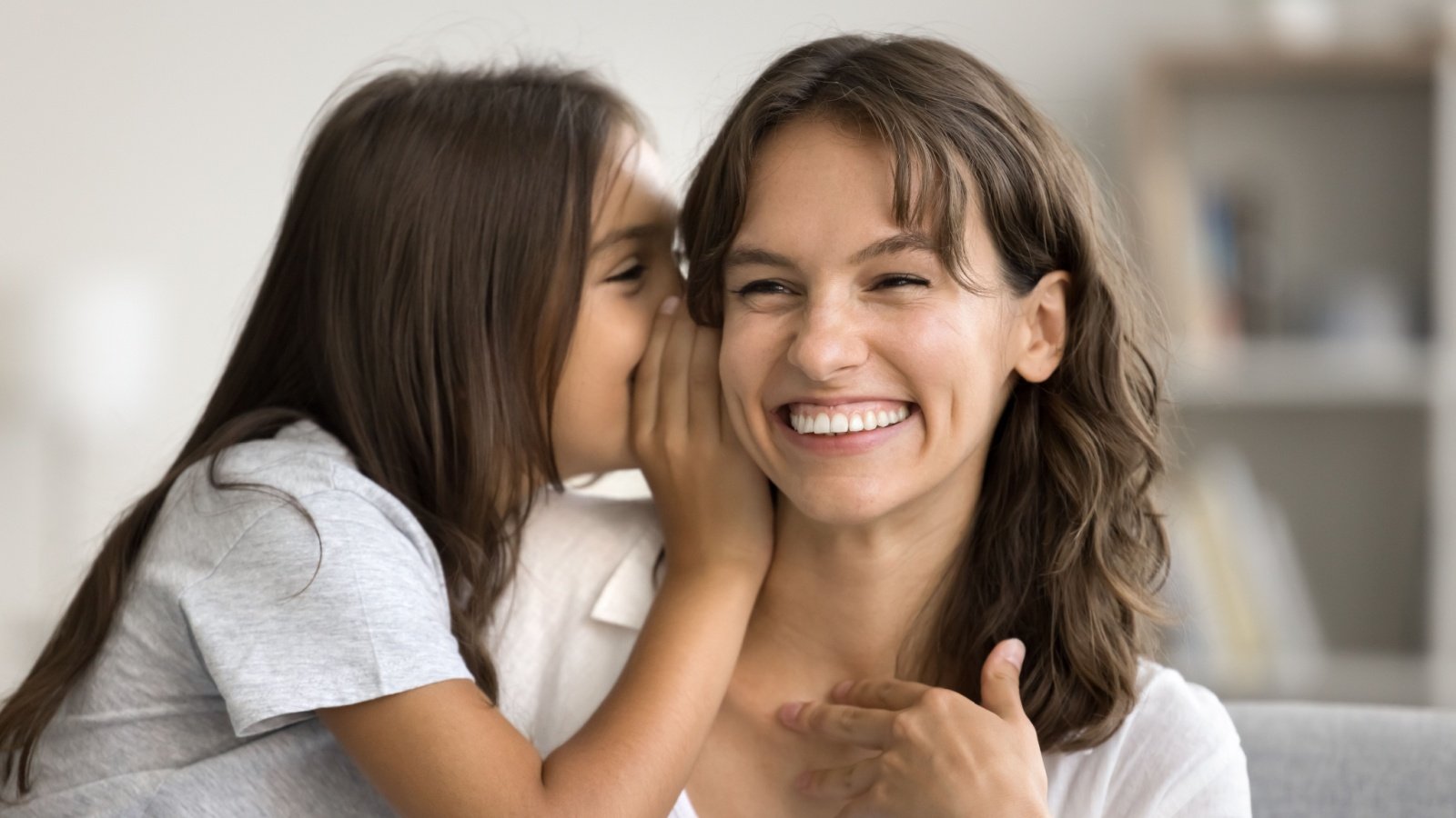 Mother and daughter telling secrets whispering smiling laughing parenting family fizkes Shutterstock