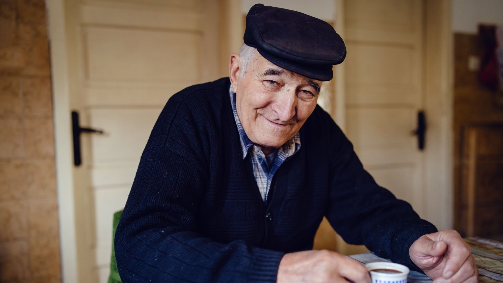 Older male wearing hat inside drinking coffee Miljan Zivkovic Shutterstock