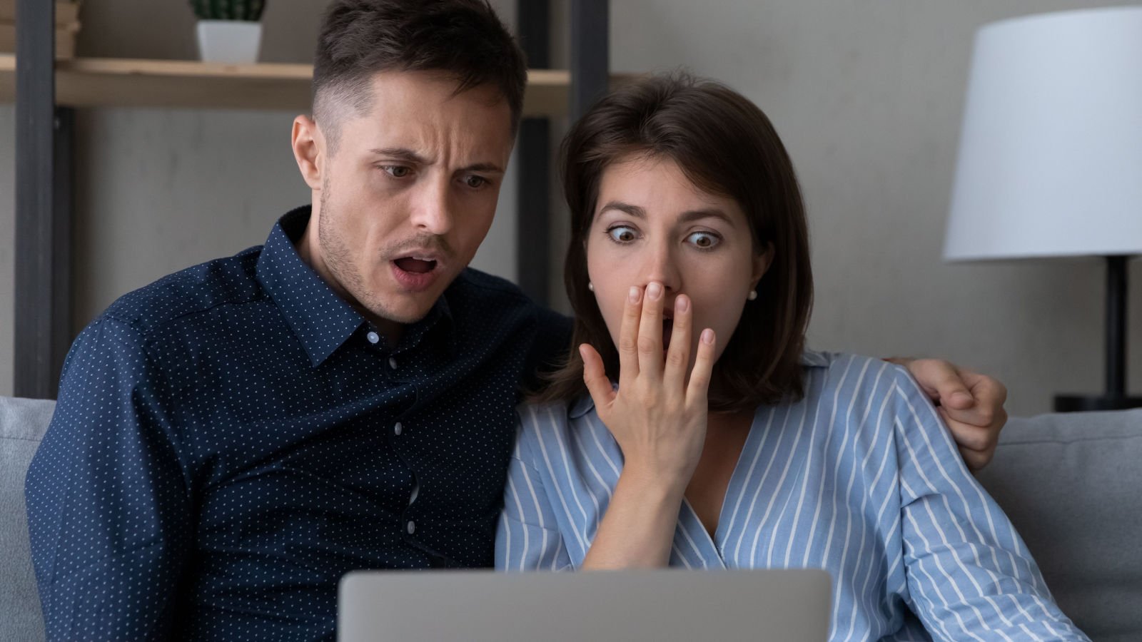 Shocked frustrated couple getting bad unexpected surprising news staring at laptop screen social media fizkes shutterstock