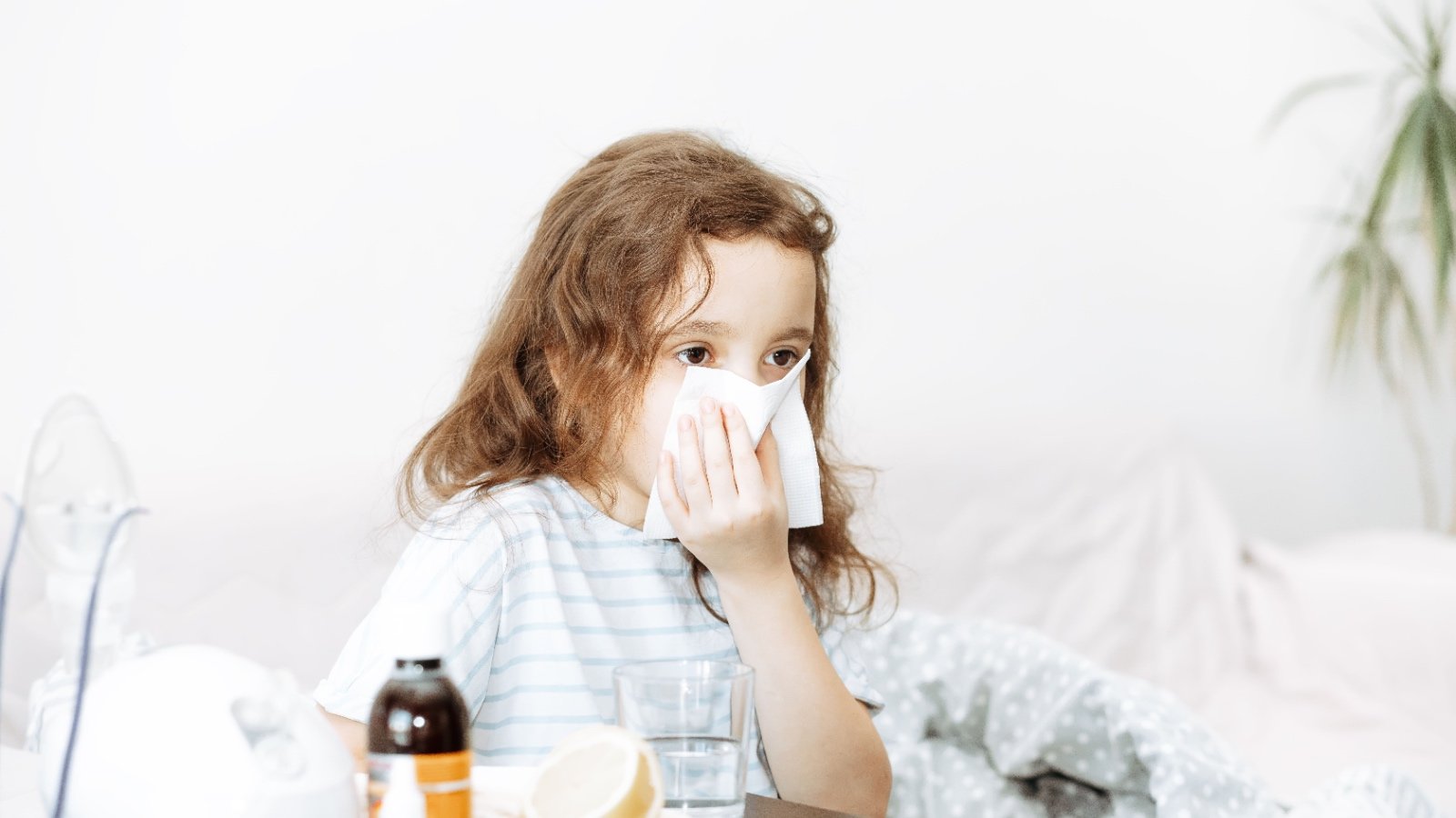 Sick little kid girl sits on bed at home and blows her nose Flu season Zulfiska Shutterstock