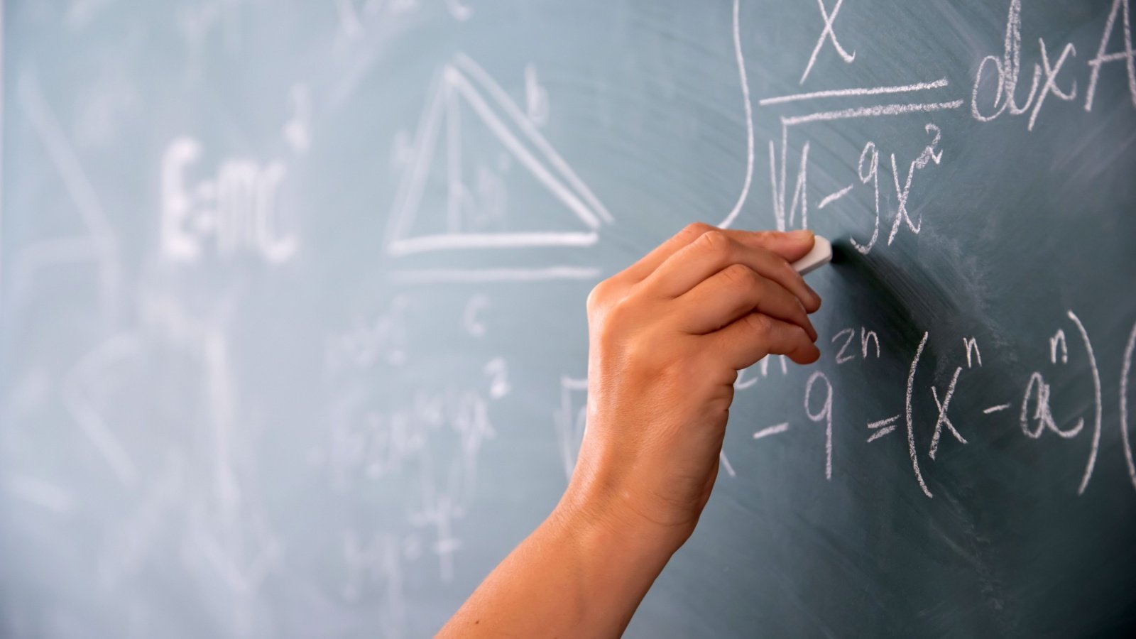 Student writing mathematical equations with chalk on the blackboard school education Melinda Nagy Shutterstock