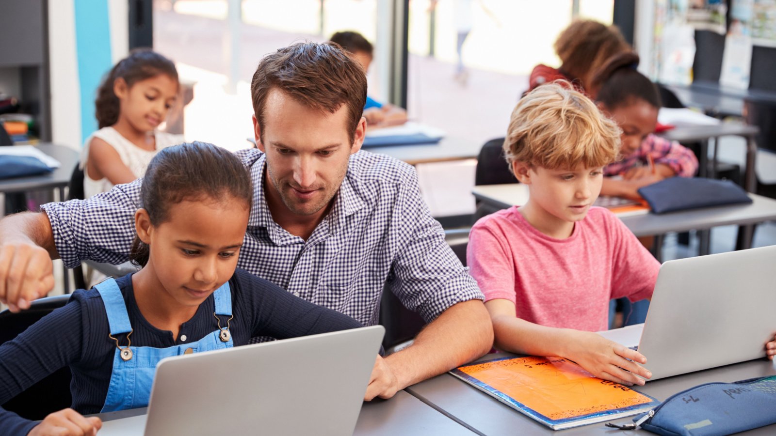 Teacher helping young students using laptops in class Monkey Business Images Shutterstock