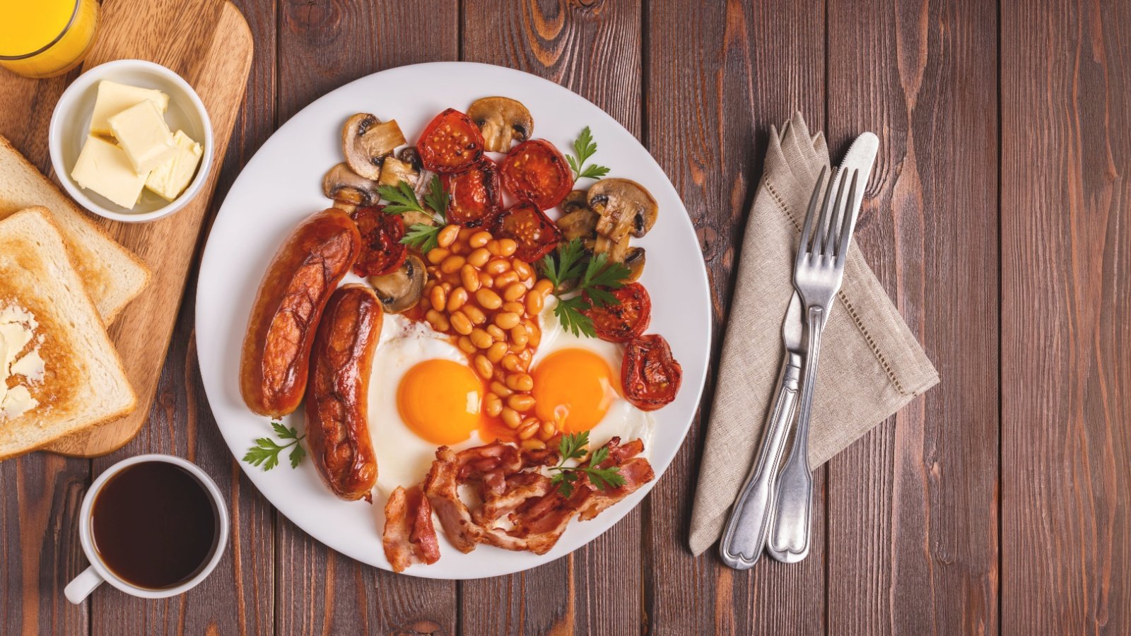 Traditional full English breakfast with fried eggs sausages baked beans mushrooms grilled tomatoes toast butter coffee and bacon Tatiana Bralnina Shutterstock