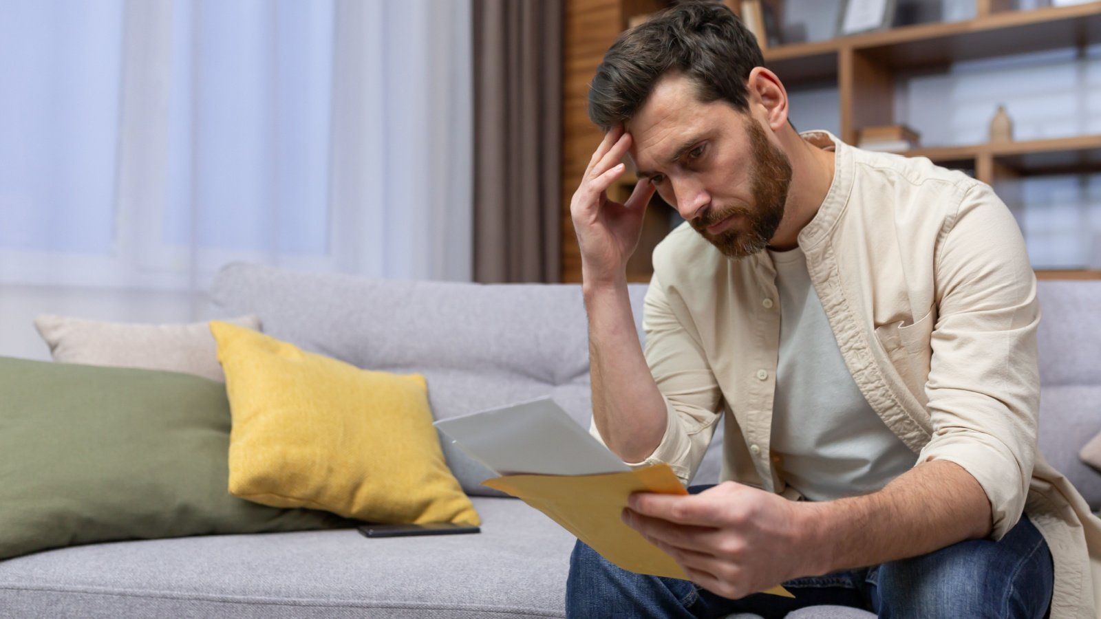 Upset male at home sitting on sofa reading letter with bad news notification in envelope opening voronaman shutterstock