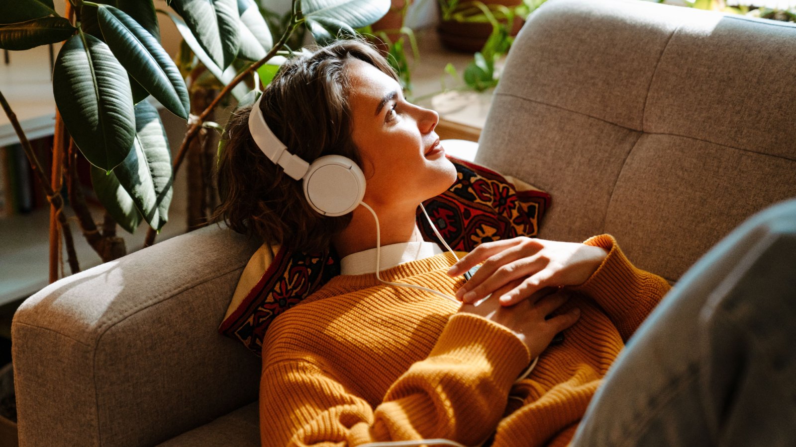 Woman listening music headphones home couch cozy Dean Drobot Shutterstock