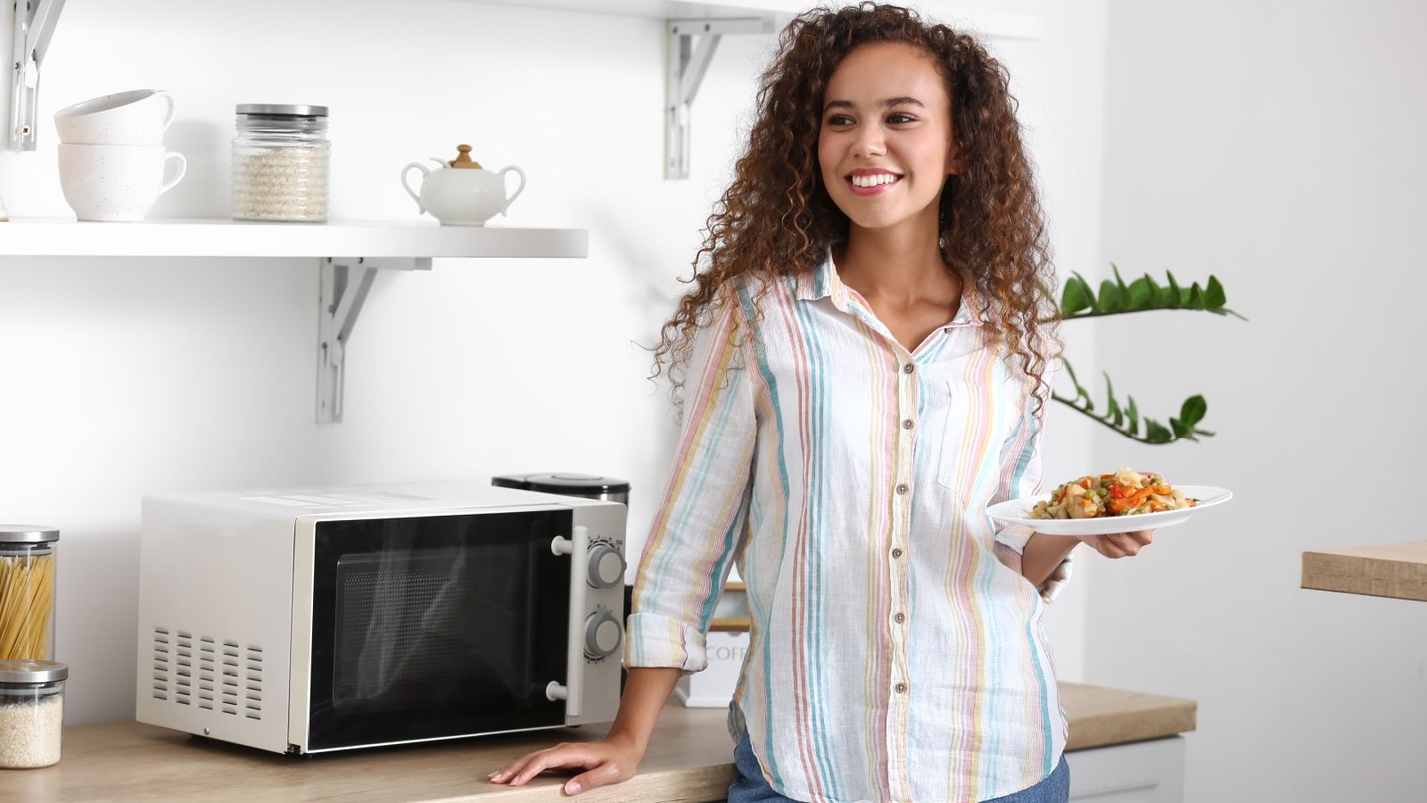 Young POC woman near microwave oven in kitchen Pixel Shot Shutterstock