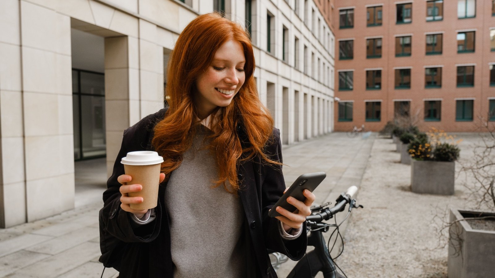 Young redheaded woman on phone with bike and coffee Dean Drobot Shutterstock