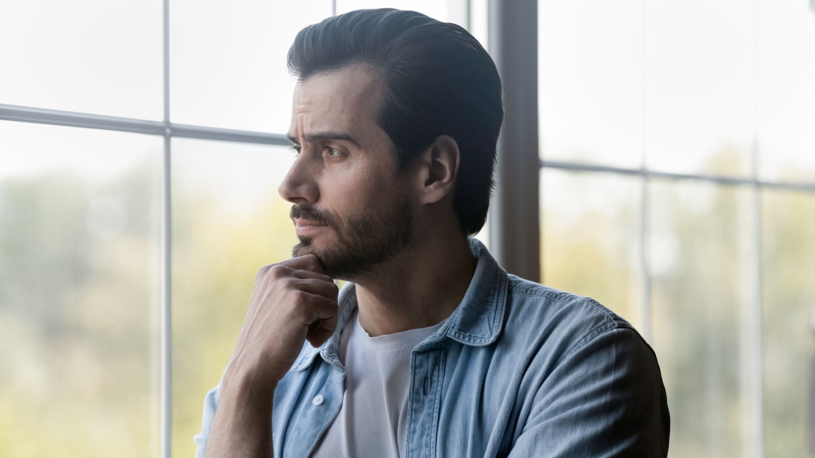 male looking out window home real estate worried pensive fizkes shutterstock