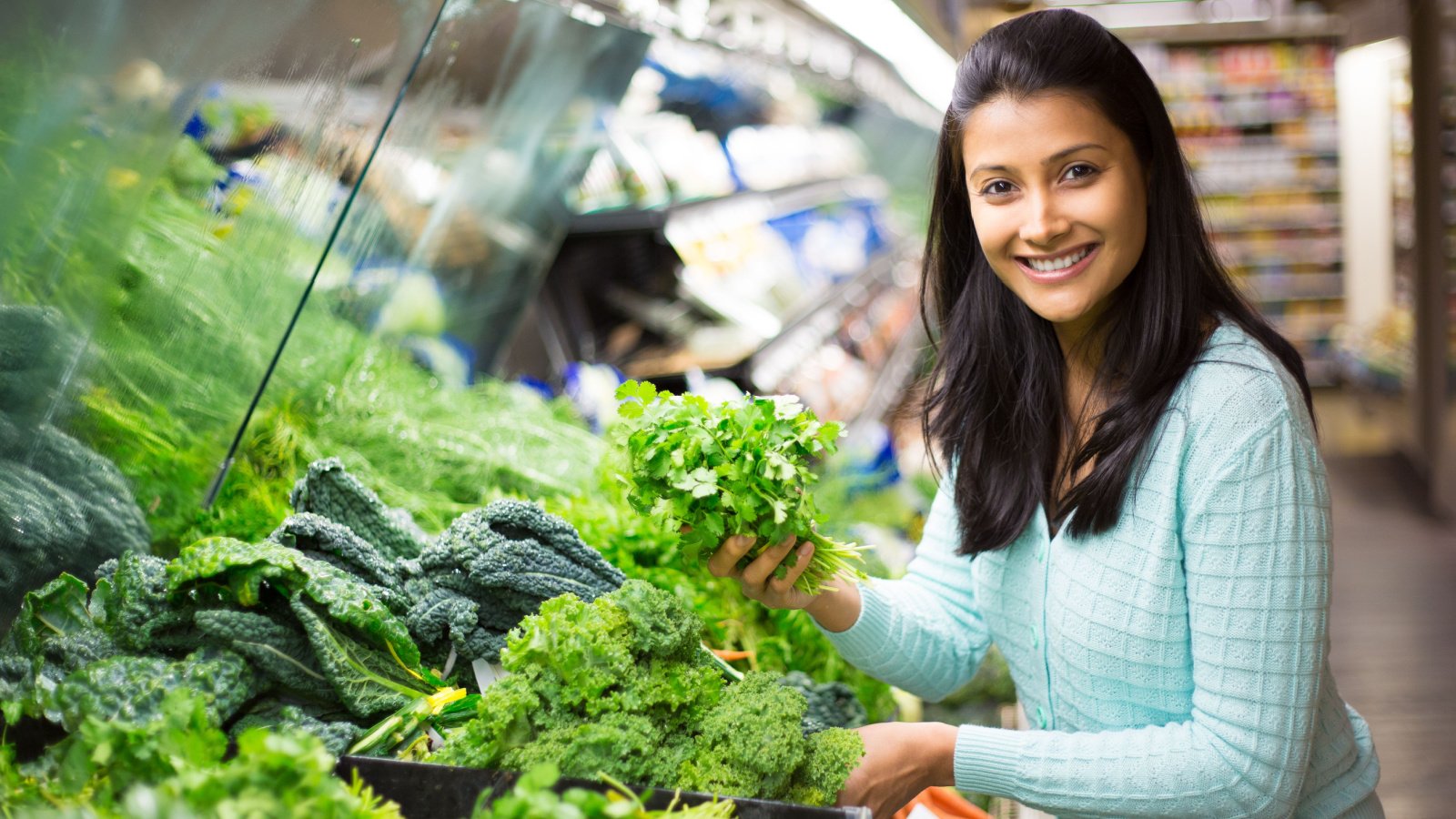 pretty young woman in sweater picking up choosing green leafy vegetables in grocery store supermarket asht productions shutterstock