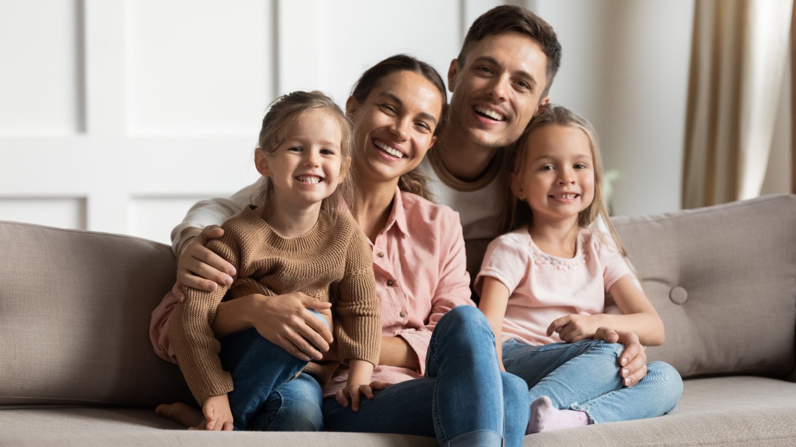 smiling parents with two little daughters sitting on couch fizkes shutterstock