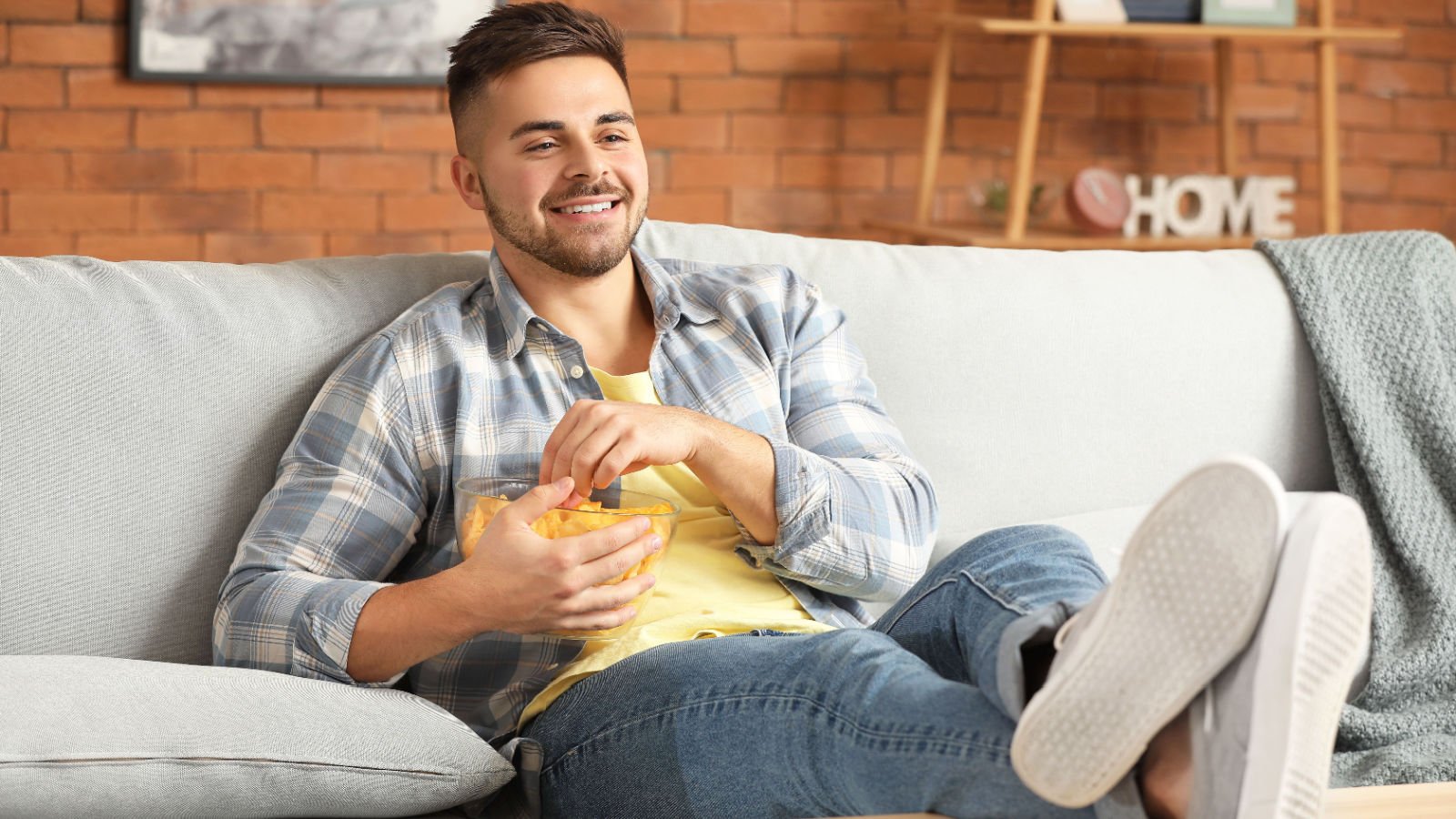 young male eating tasty potato chips while watching TV at home couch sitting pixel shot shutterstock